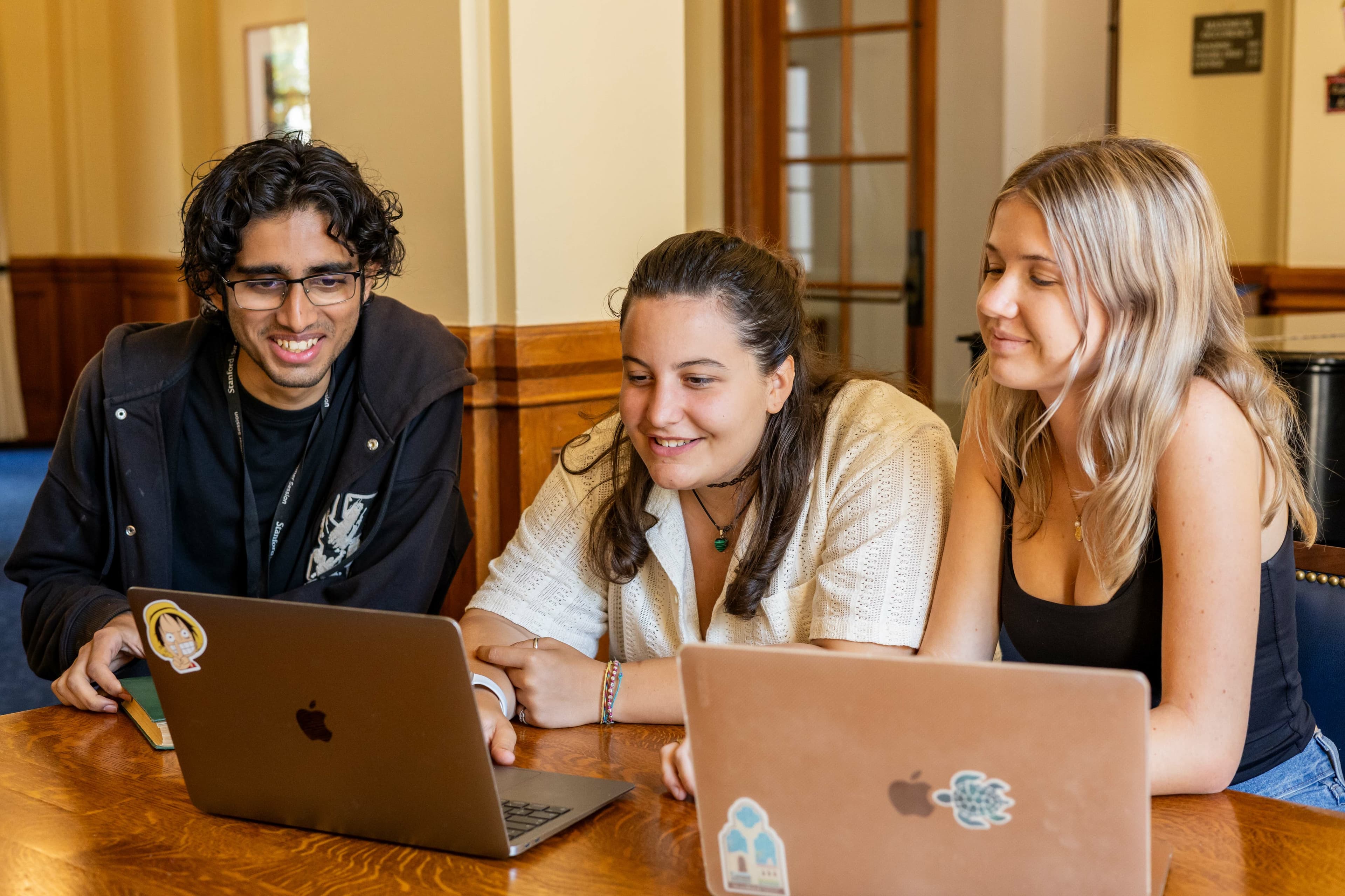 one male student and two female students looking at two laptops smiling