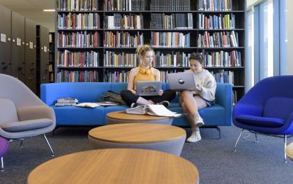 Students sit on a blue sofa in front of a shelf of books.