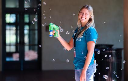 A Stanford Summer Residence Assistant stands with a bubble gun making bubbles and smiling.